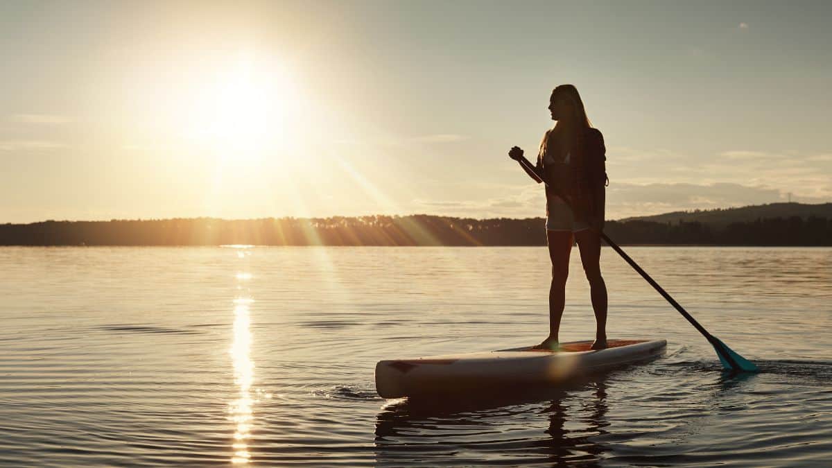 A photo of a woman standing on top of a paddle board while the sun is setting