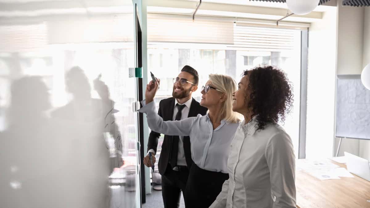 A photo of three people in an office working on a whiteboard