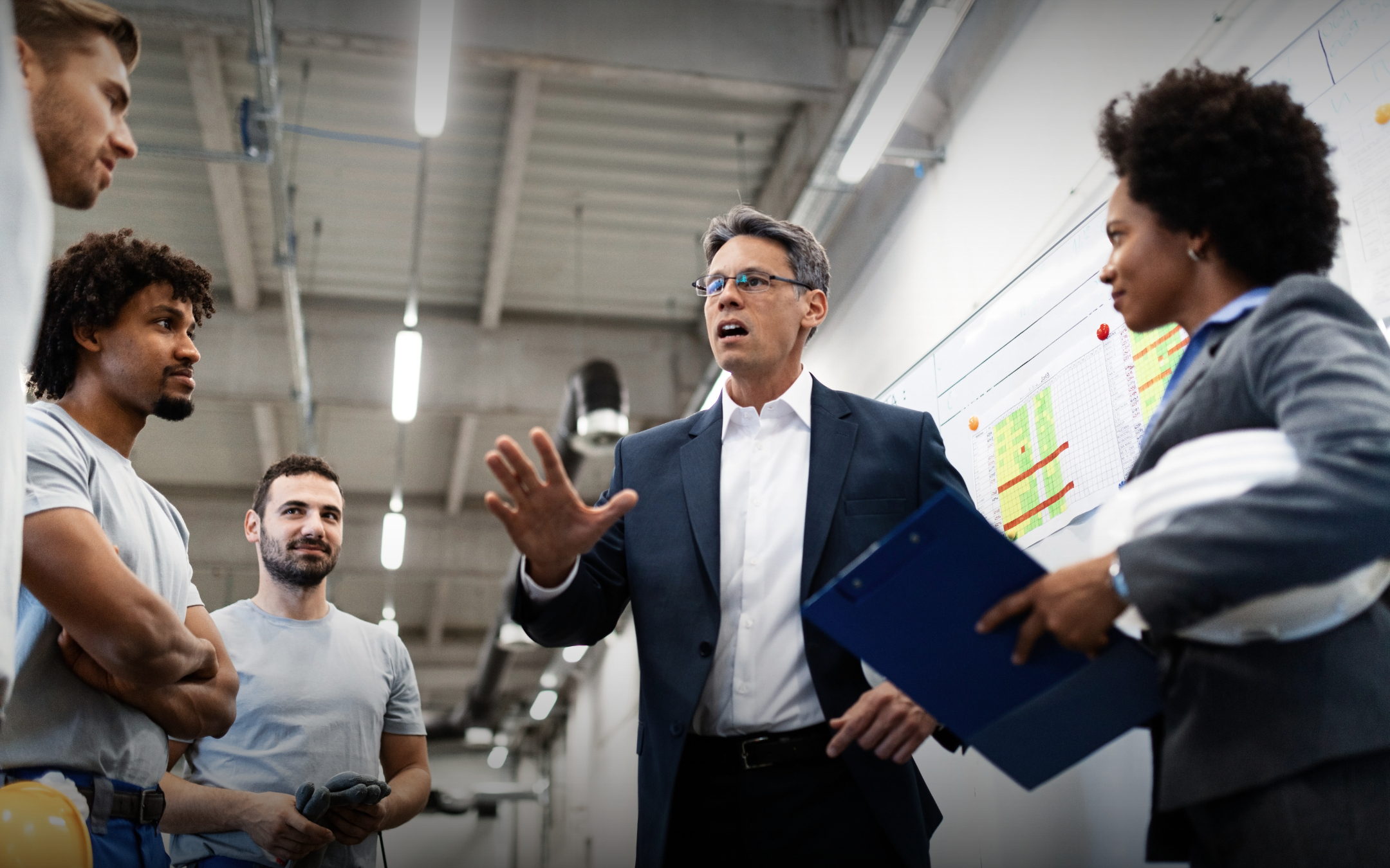 A professional leader with gray hair gestures while speaking to colleagues, appearing to be a manager or mentor in a business discussion.