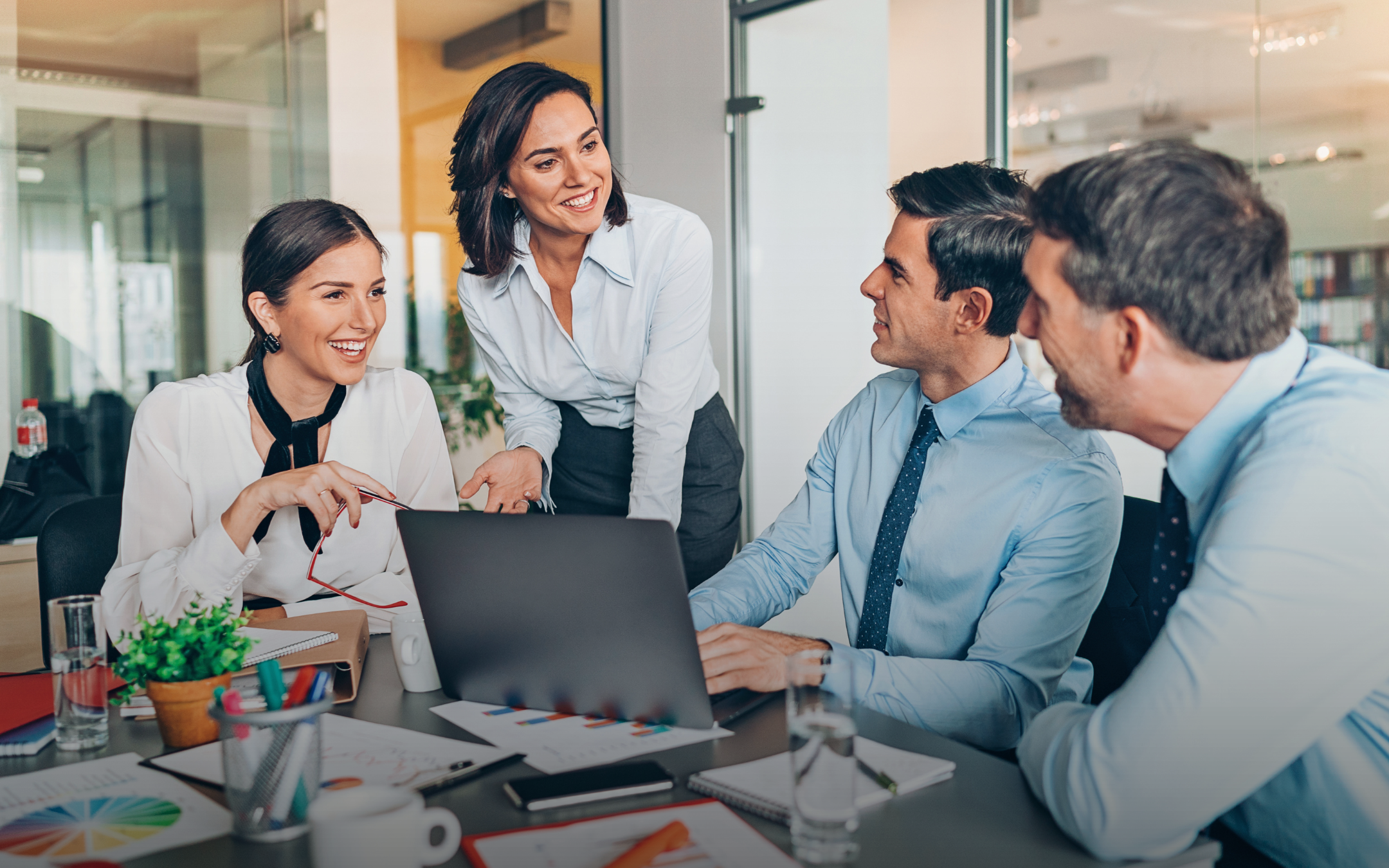 A group of business leadership executives gathered around a table with a laptop, intensely engaged in a team meeting and discussion.
