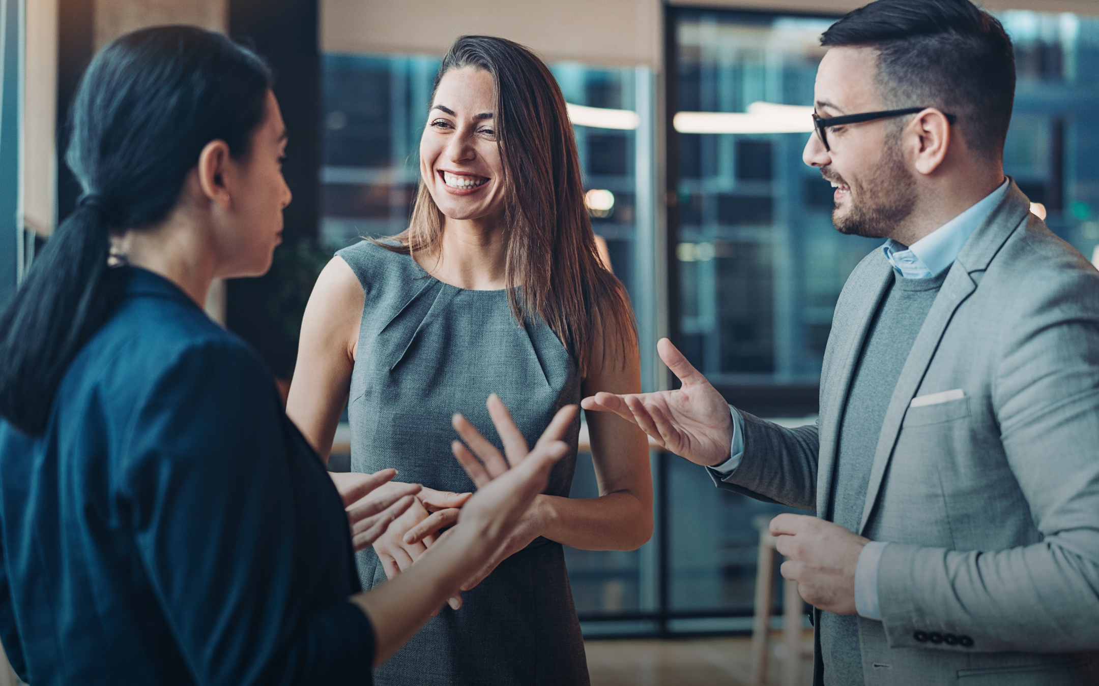 A group of diverse women is engaged in a lively and professional conversation in an office setting.
